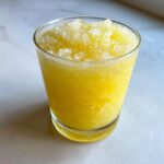 Close-up of a bright yellow lemon juice tonic slush topped with crushed ice in a clear glass.