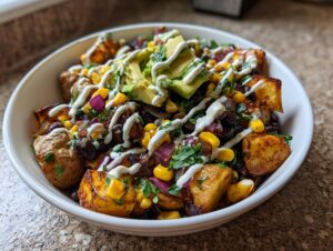 A close-up of loaded southwest potato bowls featuring roasted potatoes, black beans, corn, red onion, avocado, and a drizzle of white sauce.