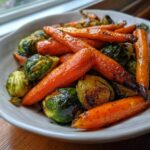 Close-up of roasted Maple Glazed Carrots and Brussels Sprouts coated in a dark, shiny glaze, served in a white bowl.