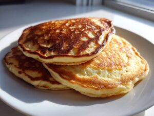 A stack of three perfectly cooked, golden-brown pancakes from scratch on a white plate.