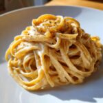 Close-up of fettuccine pasta generously coated in creamy brown butter alfredo sauce and sprinkled with black pepper.