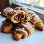 A stack of golden brown pecan pie crescents drizzled with white icing, one is cut open showing the rich pecan filling.