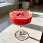 A vibrant red raspberry honey lemon daiquiri served in a coupe glass, garnished with fresh raspberries.