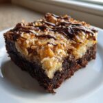 A single square of samoa brownies featuring a rich chocolate base, thick caramel-coconut topping, and a chocolate drizzle.