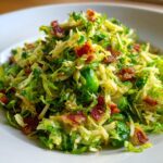 A mound of vibrant Sautéed Shredded Brussels Sprouts mixed with crispy bacon bits served on a white plate.