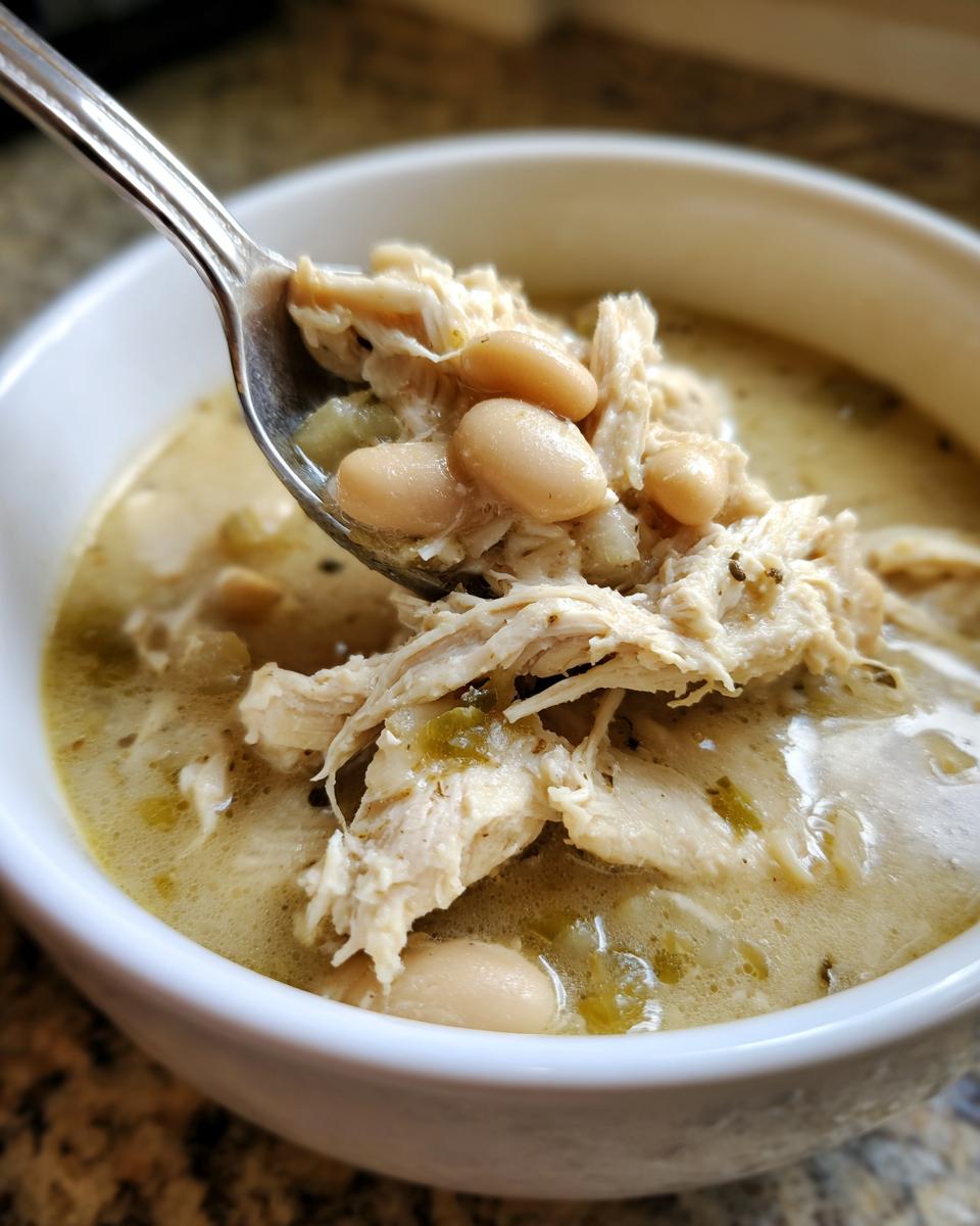 A spoonful lifted from a bowl showing shredded chicken and white beans in creamy crockpot white chicken chili.