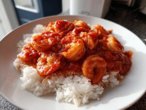 A close-up of a white plate piled high with fluffy white rice topped generously with rich, red sauce shrimp creole.
