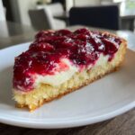Close-up of a slice of cherry dessert pizza featuring a thick cake base, white cream filling, and bright red cherry topping.