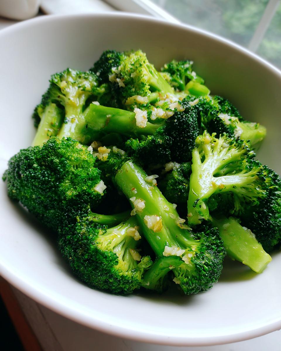 Close-up of bright green steamed broccoli florets tossed with minced garlic in a white bowl.