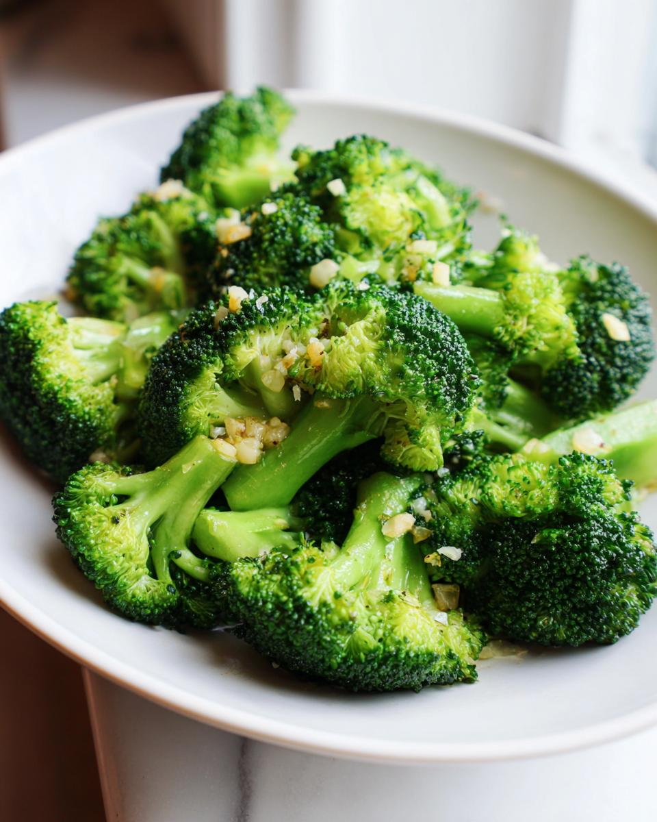 Close-up of bright green steamed broccoli florets tossed with minced garlic in a white bowl.
