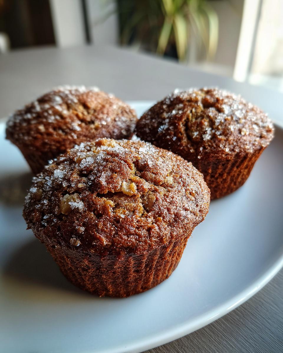 Three freshly baked banana nut muffins topped with coarse sugar crystals, resting on a white plate.