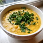 Close-up of a thick, yellow chickpea soup topped generously with fresh chopped parsley.