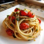 A close-up of a serving of tomato basil pasta, featuring spaghetti tossed with roasted cherry tomatoes and fresh basil.