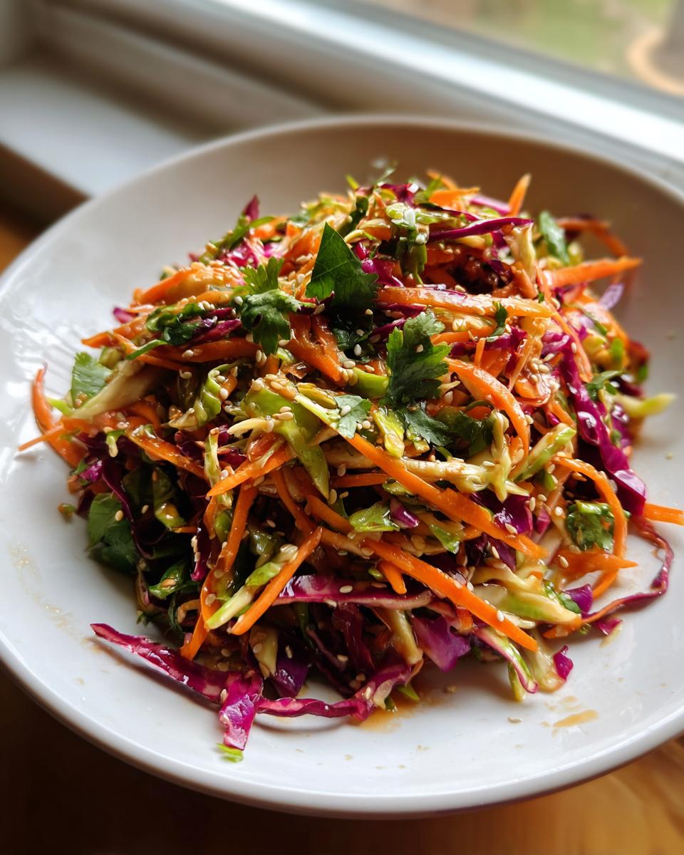A close-up of vibrant Asian cabbage slaw featuring shredded carrots, red cabbage, and cilantro, topped with sesame seeds.