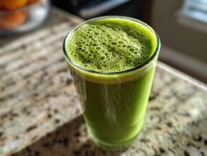 Close-up of a vibrant green fat burning smoothie with foamy bubbles on top, sitting on a granite countertop.