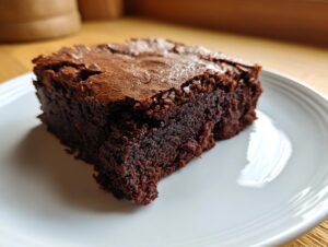 Close-up of a fudgy slice of zero sugar brownies with a crackly top, served on a white plate.
