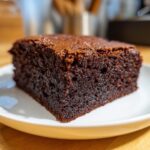A close-up of a rich, dark, moist slice of zero sugar brownies resting on a white plate.
