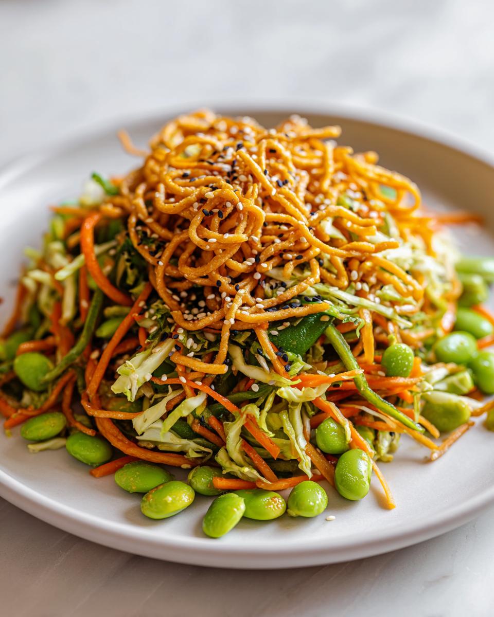 A vibrant Asian edamame salad featuring shredded carrots, cabbage, bright green edamame, and topped with crispy chow mein noodles and sesame seeds.