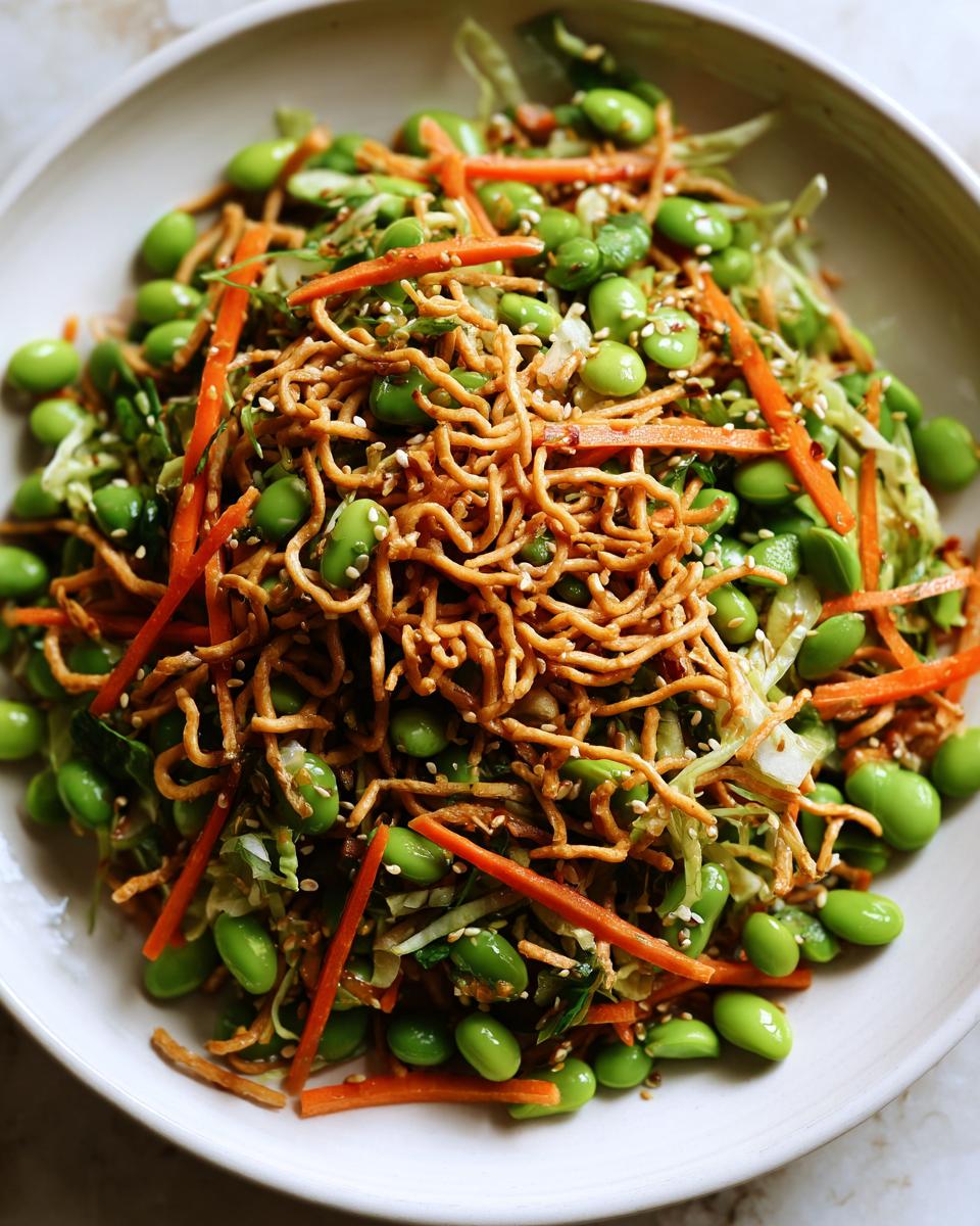 Close-up of a vibrant Asian edamame salad featuring bright green edamame, shredded carrots, cabbage, and crispy chow mein noodles.