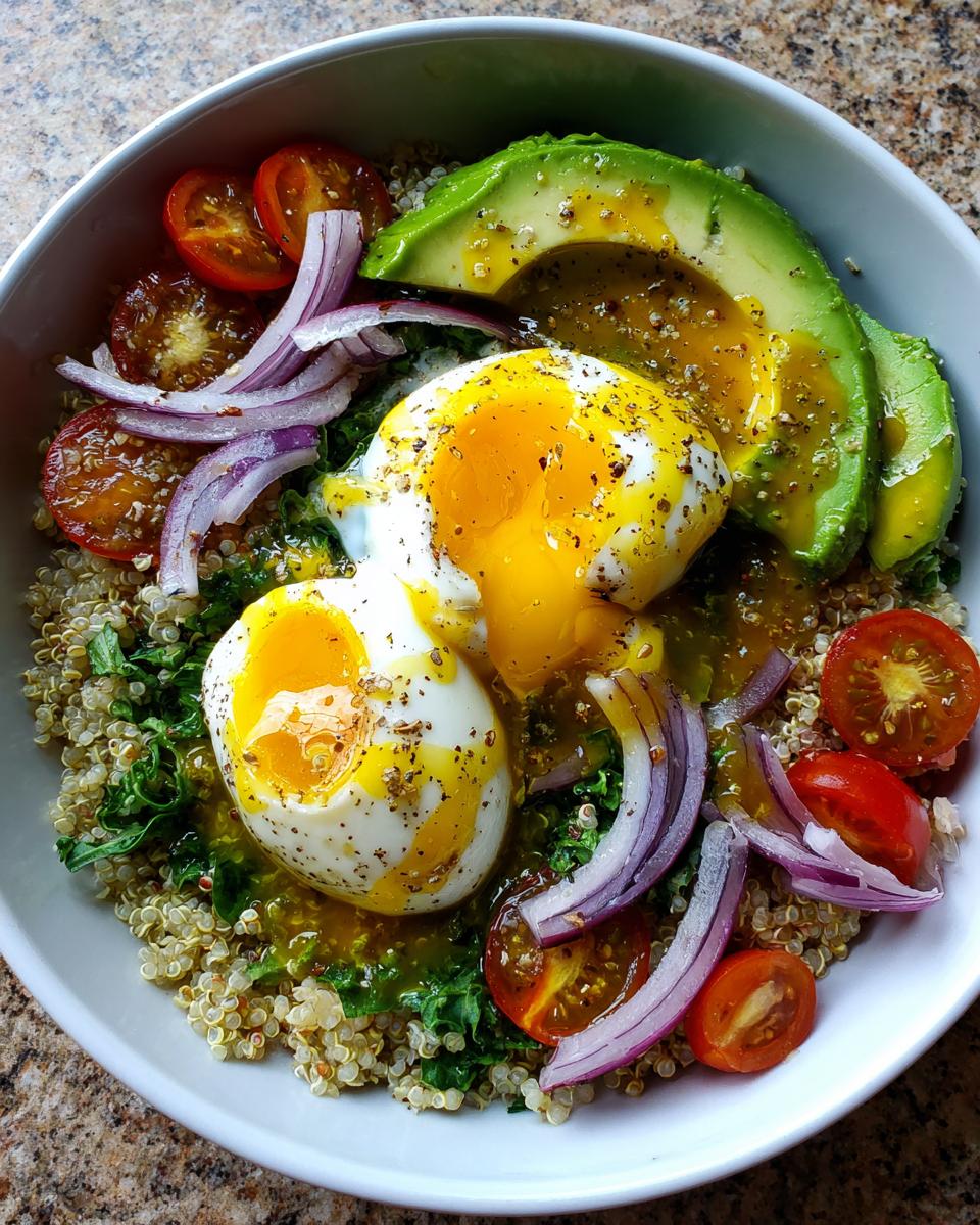 A vibrant avocado egg quinoa bowl featuring two soft-boiled eggs with runny yolks, sliced avocado, red onion, and tomatoes.