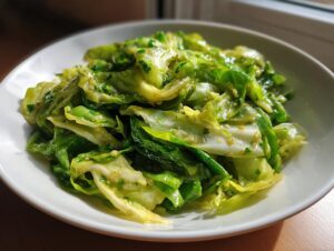 A close-up of a vibrant green cabbage saute, glistening with sauce and herbs, served in a white bowl.