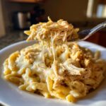 A fork lifts shredded, cheesy crockpot olive garden chicken mixed with penne pasta, showing long cheese pulls.