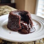 A rich, dark chocolate lava cake cut open to show the gooey, molten center flowing onto a white plate.