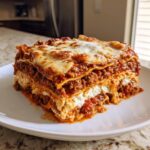 A generous slice of classic homemade lasagna showing layers of meat sauce, ricotta, and melted mozzarella cheese.