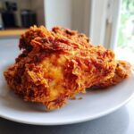 Close-up of golden-brown, extra crispy buttermilk fried chicken stacked on a white plate.