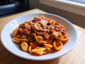 A white bowl filled with rich ground beef orecchiette pasta topped with grated cheese.