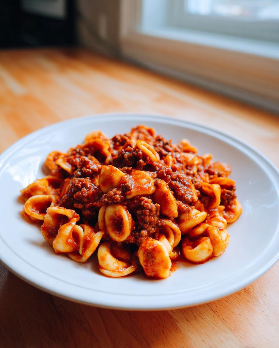 A white plate filled with delicious ground beef orecchiette pasta tossed in a rich red tomato sauce.