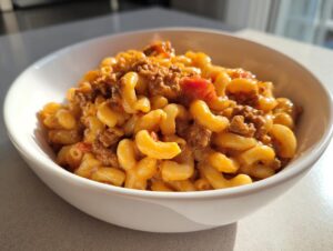A close-up of a white bowl filled with creamy, cheesy homemade hamburger helper mixed with ground beef and tomatoes.