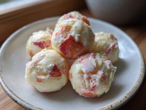 A close-up of five perfectly formed lobster crab butter bombs resting on a light-colored ceramic plate.