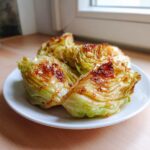 Four wedges of caramelized oven garlic cabbage served on a white plate.