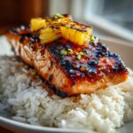 Close-up of a perfectly glazed pineapple salmon fillet resting on a bed of fluffy white rice, topped with grilled pineapple chunks.