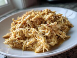 A close-up of creamy, shredded crockpot olive garden chicken served on a white plate.