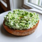 A toasted bagel half generously topped with bright green spinach cottage cheese spread, ready for a spinach cottage cheese bagel breakfast.