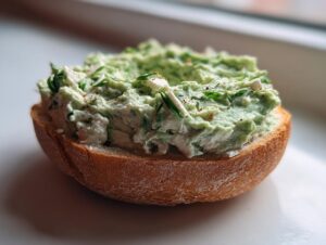 Close-up of a toasted bagel half topped generously with green spinach cottage cheese spread for a quick breakfast.