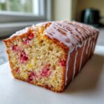 A close-up of a moist slice of strawberry lemonade bread, topped with white glaze and coarse sugar.