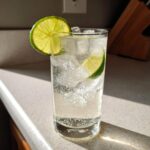 A tall glass filled with ice, clear liquid, and lime slices, representing a vanilla vodka soda.