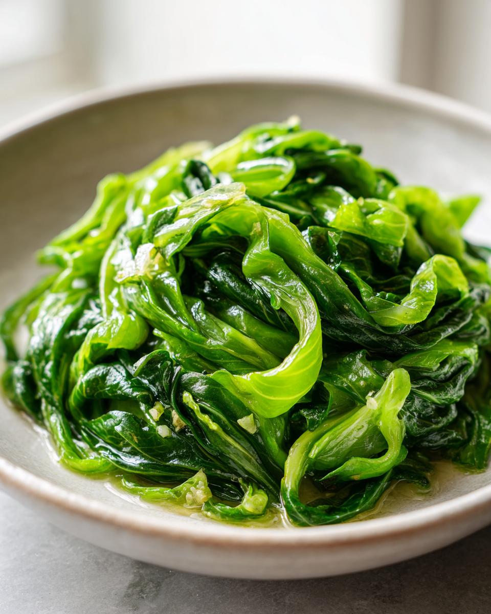 Close-up of vibrant green cabbage saute, glistening with oil and small pieces of garlic.