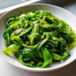 Close-up of vibrant green cabbage saute, thinly sliced and glistening with garlic and oil.